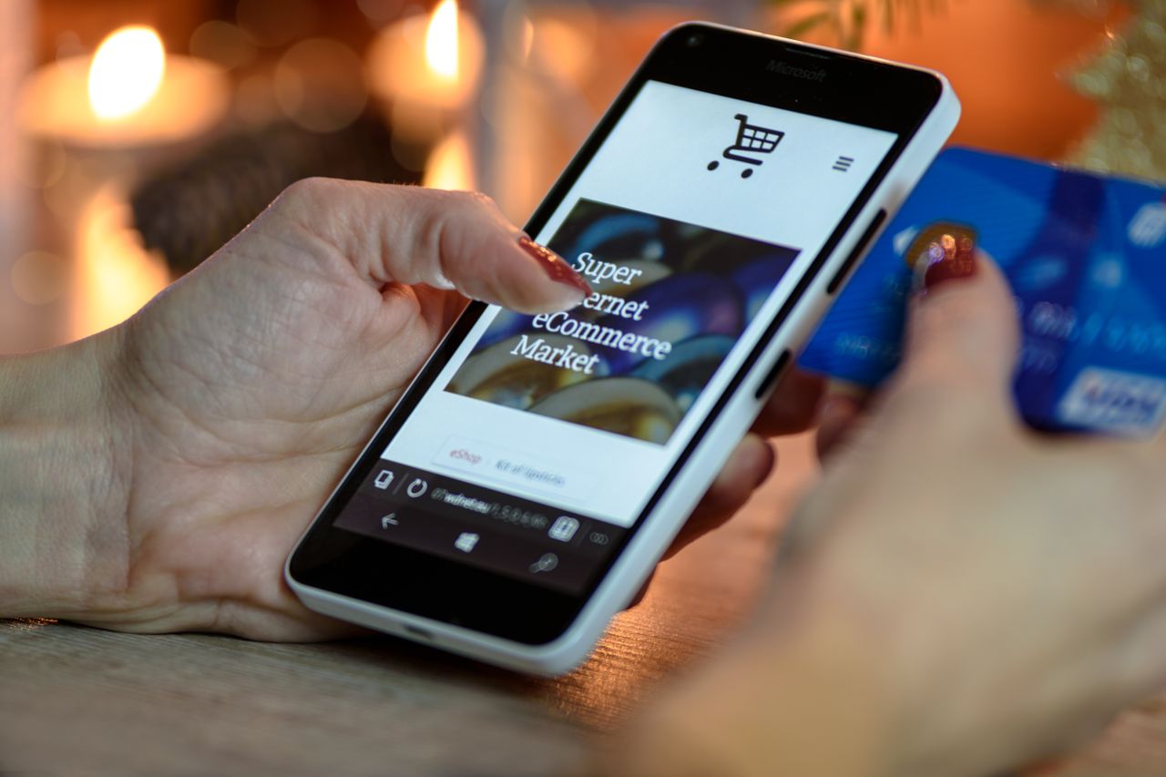 category-03 Woman using smartphone for online shopping with credit card in hand, festive background lighting.